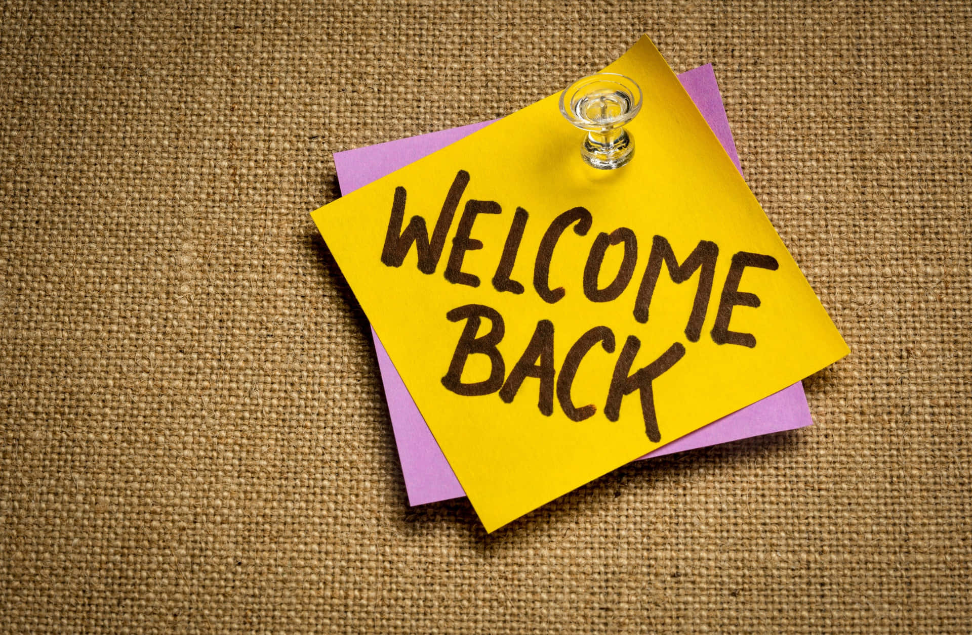  壁紙 — 一張黃色便利貼，上面手寫著「WELCOME BACK」，釘在帶有紋理的黃麻表面上。