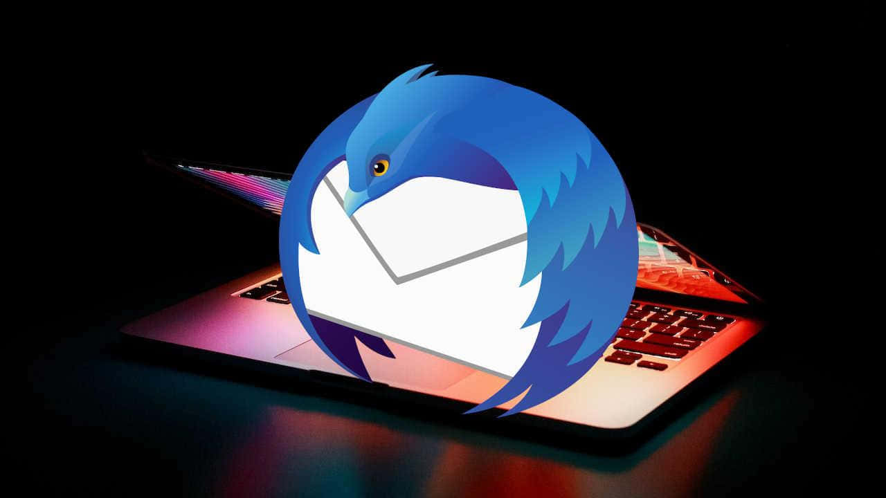  壁紙 — 一隻風格化的藍鳥拿著信封從發光的筆記型電腦中出現，背景為深色。