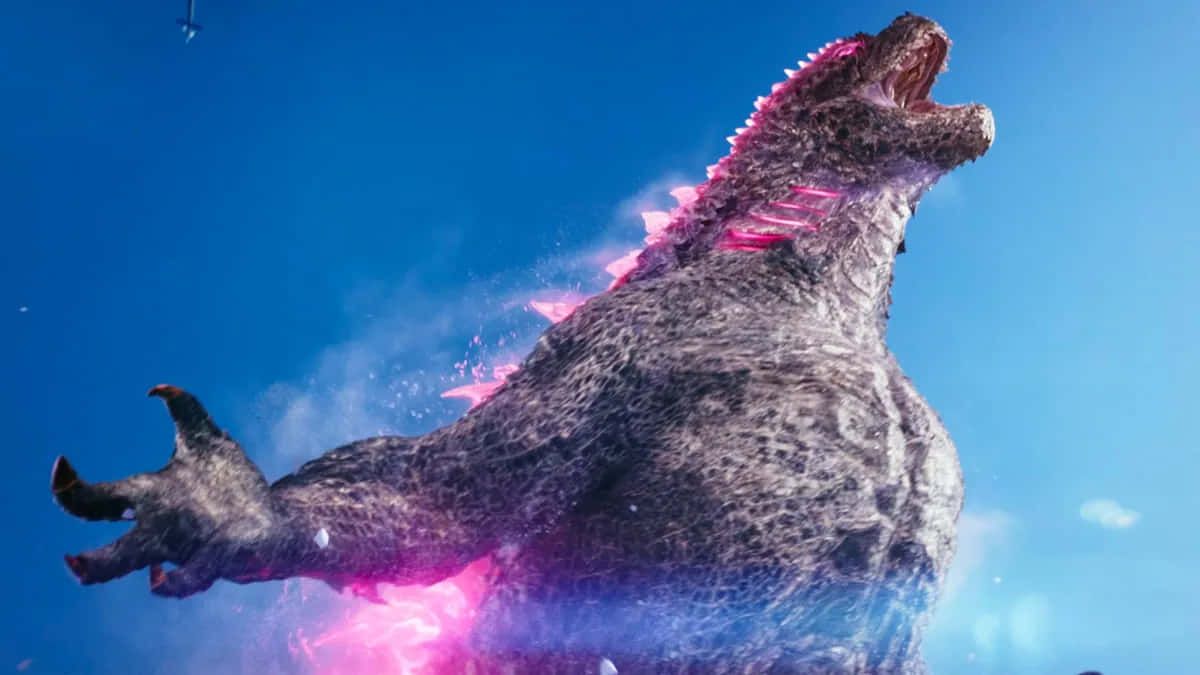 Godzilla X Kong The New Empire 桌布 壁紙 — 一隻巨大的哥斯拉對著晴朗的藍天咆哮，粉紅色的能量沿著牠的脊椎劈啪作響並從胸口噴發出來。