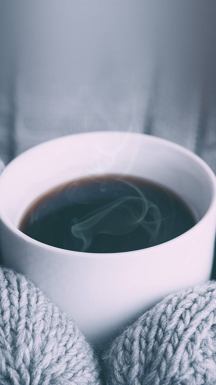 灰色針織手套的手捧著一杯冒著蒸氣的咖啡。