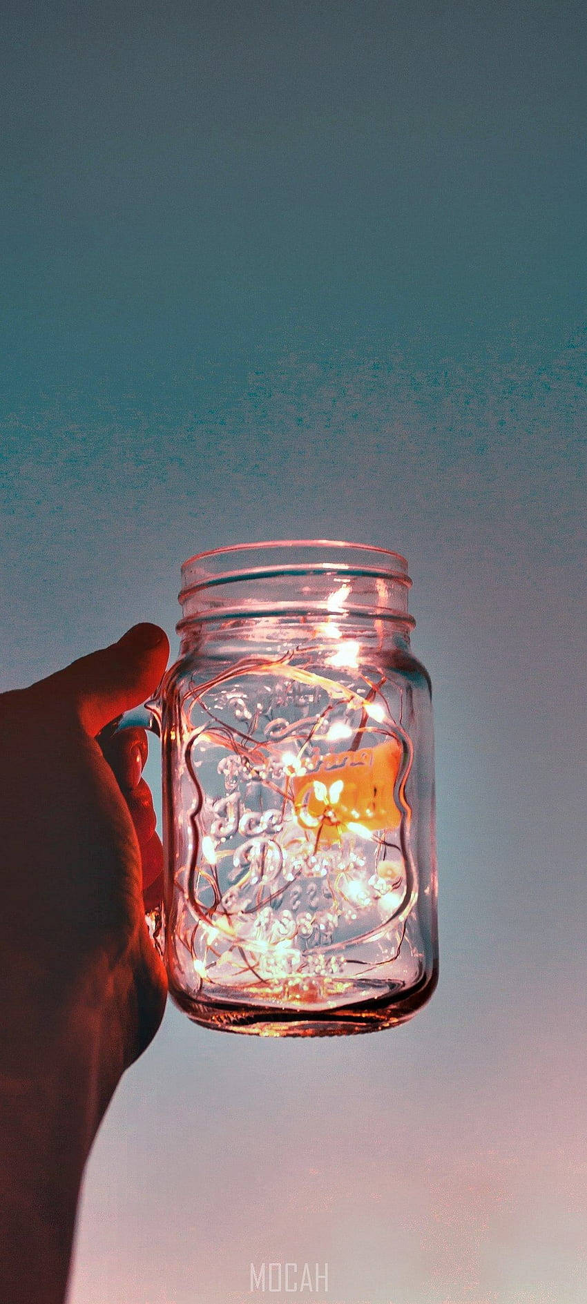 手拿著一個裝有發光燈的罐子，背景是暮色天空