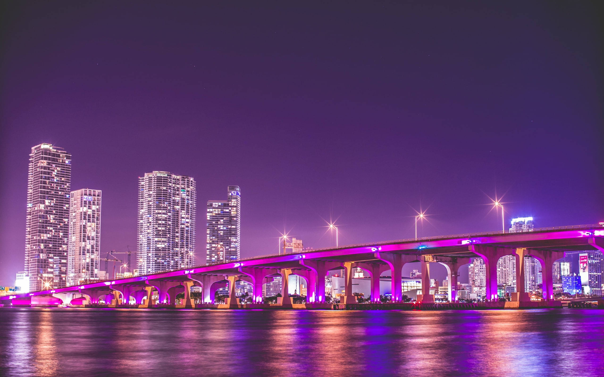 一座燈光明亮的橋樑橫跨水面，城市摩天大樓在夜晚閃爍。