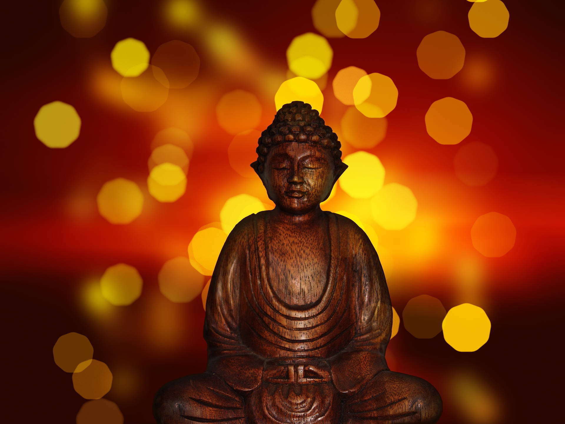發光的靈性存在 壁紙 — 一尊寧靜的木製佛像在溫暖的散景背景中冥想，背景是閃爍的琥珀色和紅色燈光。