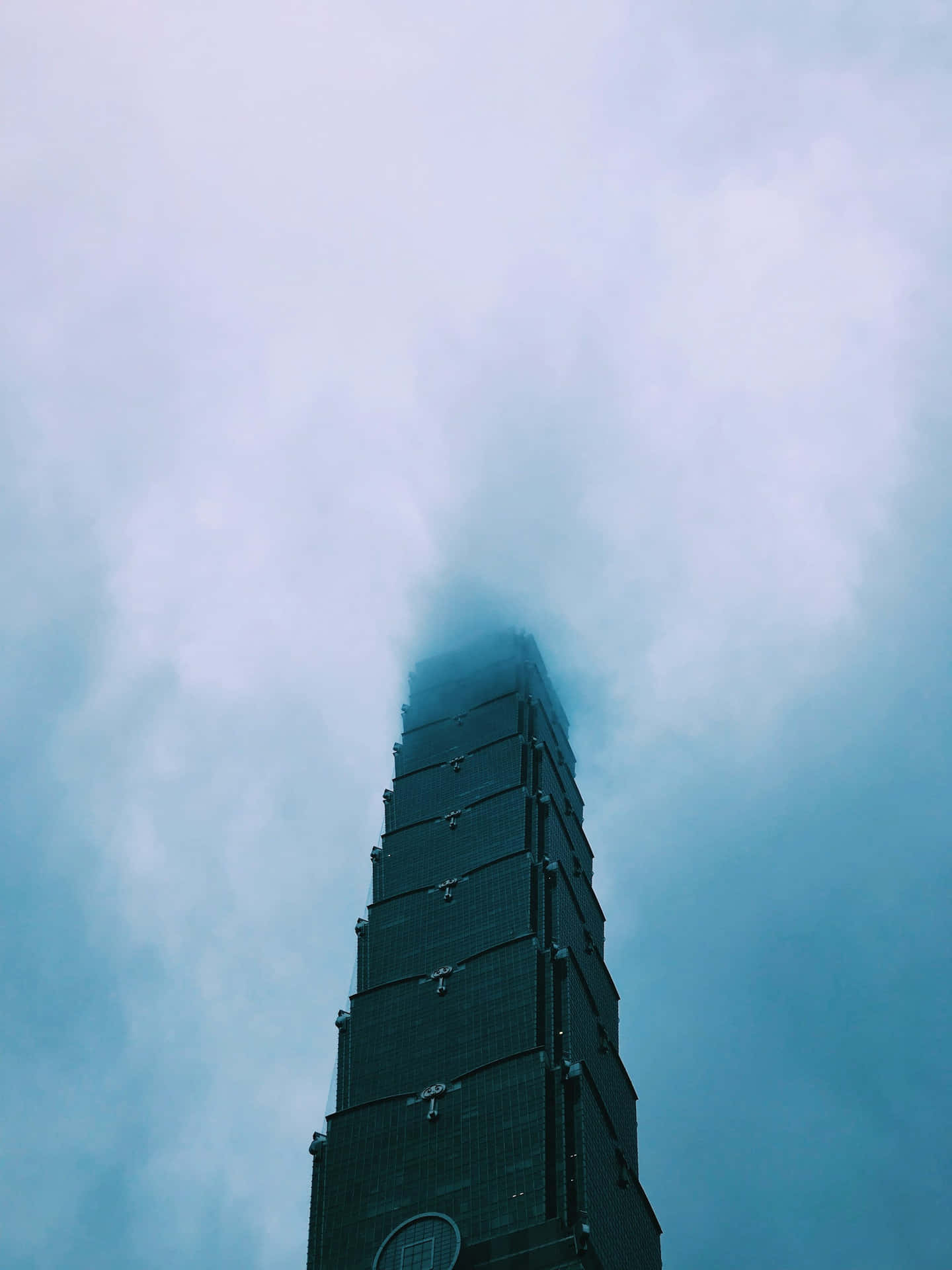  壁紙 — 一座高聳入雲的摩天大樓在清涼的藍天下穿透迷濛的雲層。