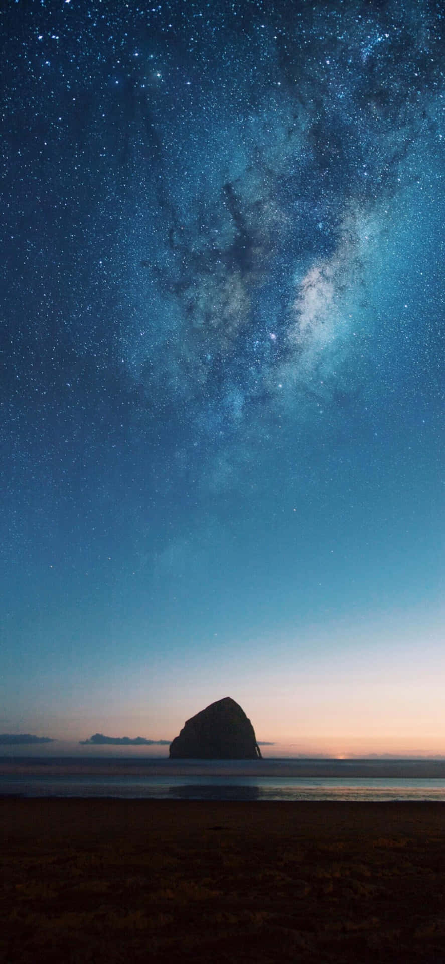  壁紙 — 一座雄偉的海蝕柱在佈滿銀河和散落星辰的暮色天空中呈現剪影。
