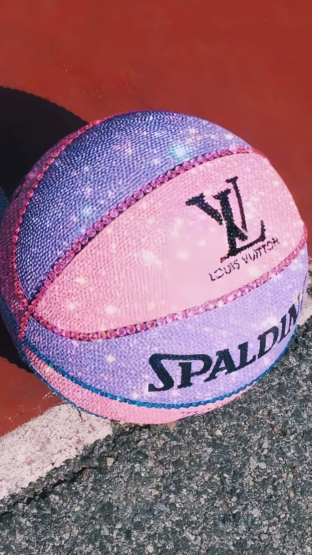  壁紙 — 一個帶有 Louis Vuitton 品牌標誌的閃粉粉紫色籃球，在明亮的陽光下放在一個破裂的瀝青球場上。
