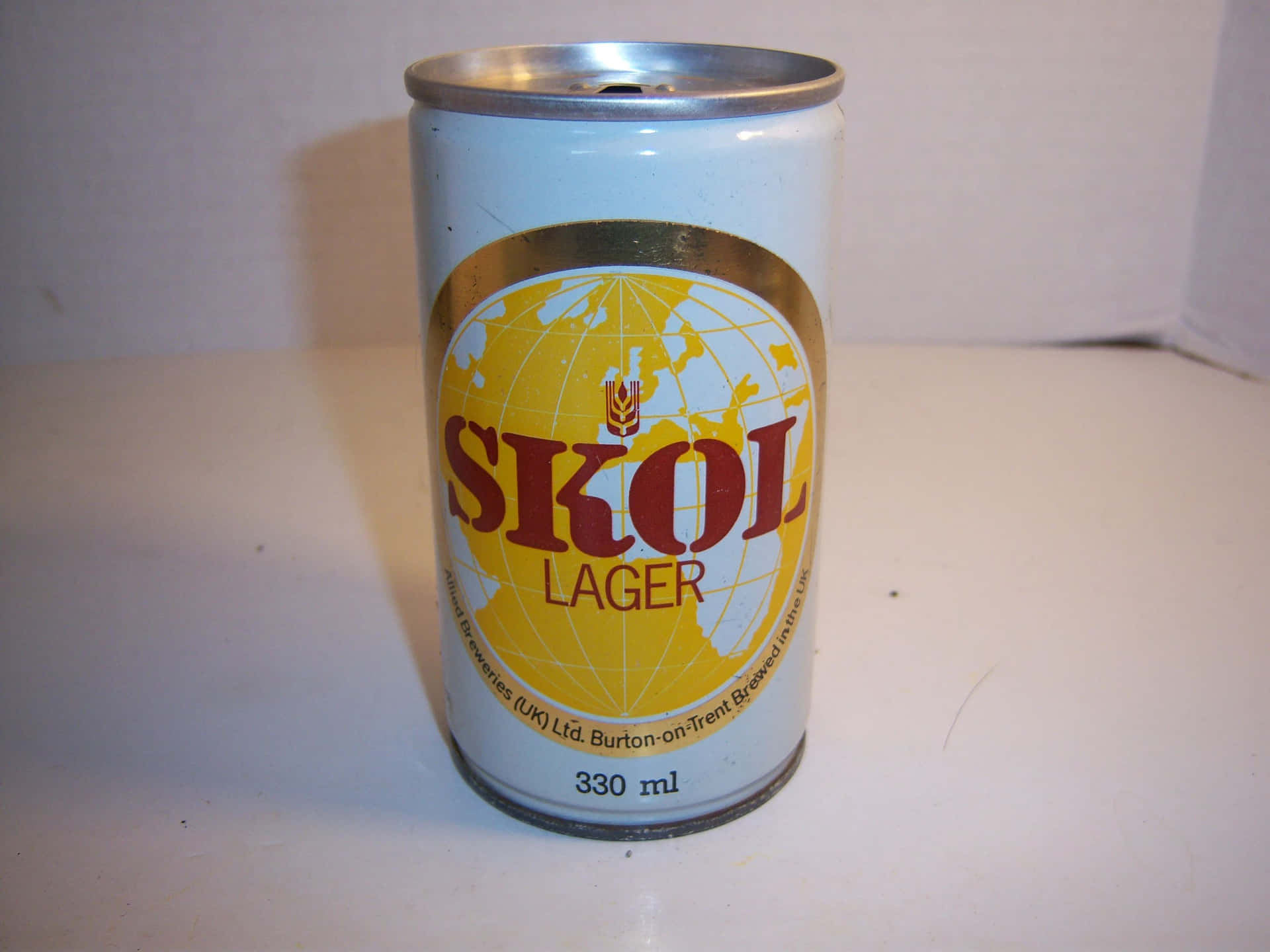  壁紙 — 一個帶有黃色地球標誌的復古Skol Lager罐子，在柔和光線下直立於純白表面上。