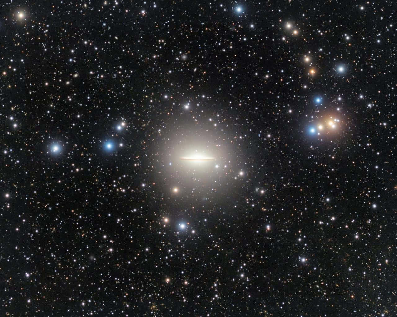  壁紙 — 一個發光的螺旋星系在充滿無數閃爍星星的星場中心發光，背景是深邃的黑色虛空。