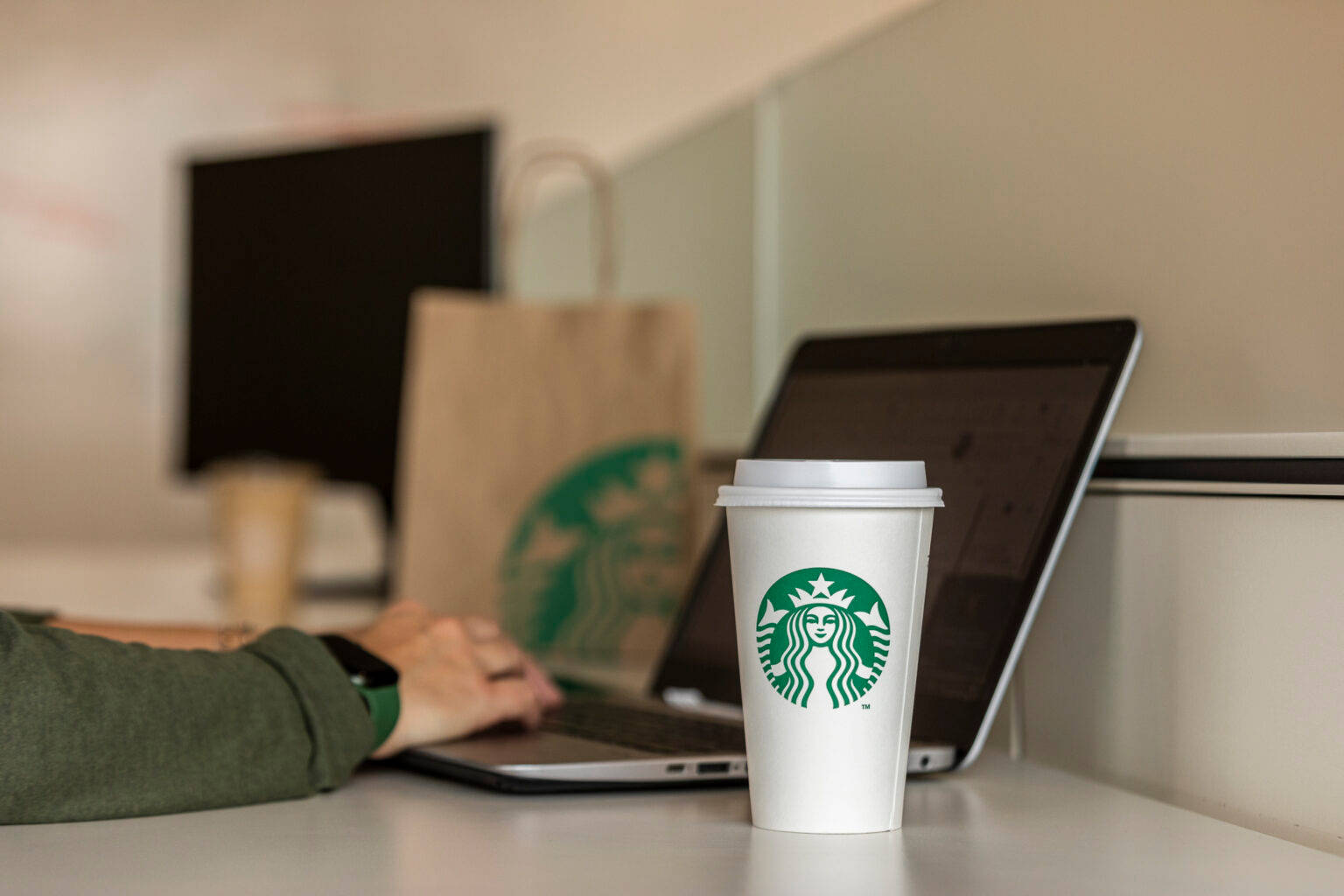 桌上一個Starbucks咖啡杯，旁邊有手提電腦，一個人在打字。