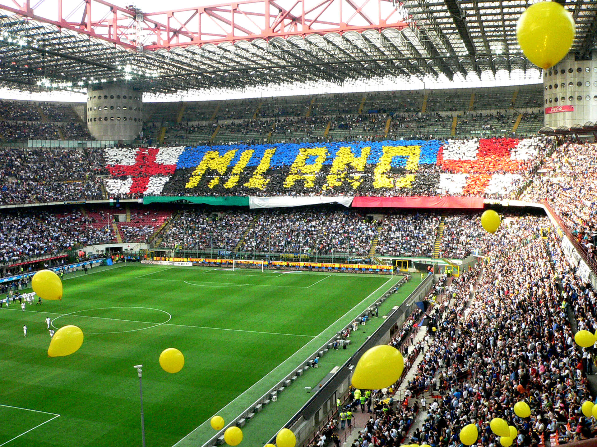  壁紙 — 一個擠滿球迷的足球場，球迷們組成巨大的「MILANO」橫幅，黃色氣球漂浮在綠色球場上方。