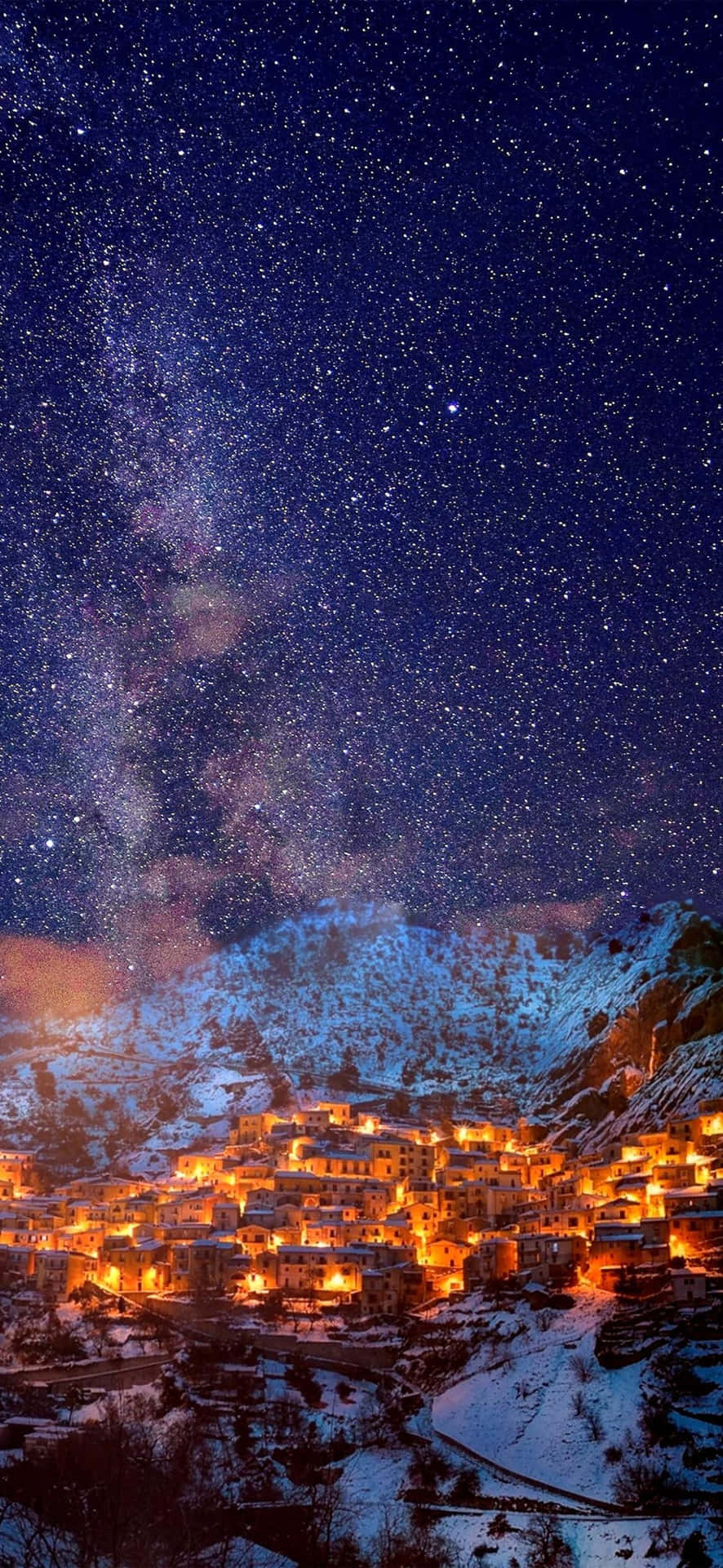  壁紙 — 一個被雪覆蓋的山村在壯麗的星空下溫暖地發光，銀河拱橋般橫跨其上。