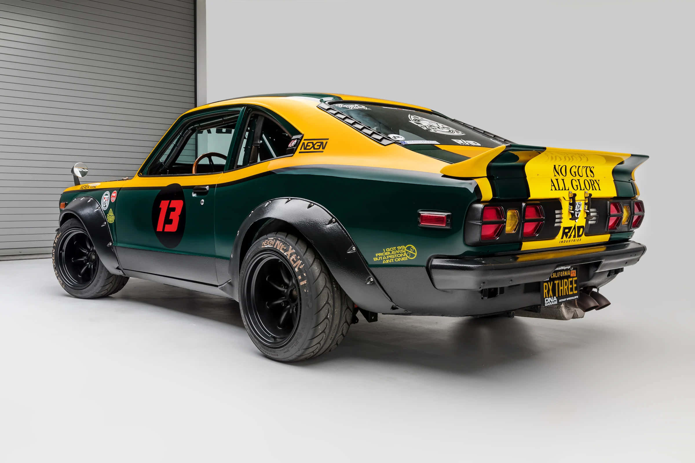 Mazda Rx-3 桌布 壁紙 — 一架充滿活力的綠色和黃色賽車，帶有13號和「No Guts All Glory」文字，在乾淨的車庫環境中拍攝。