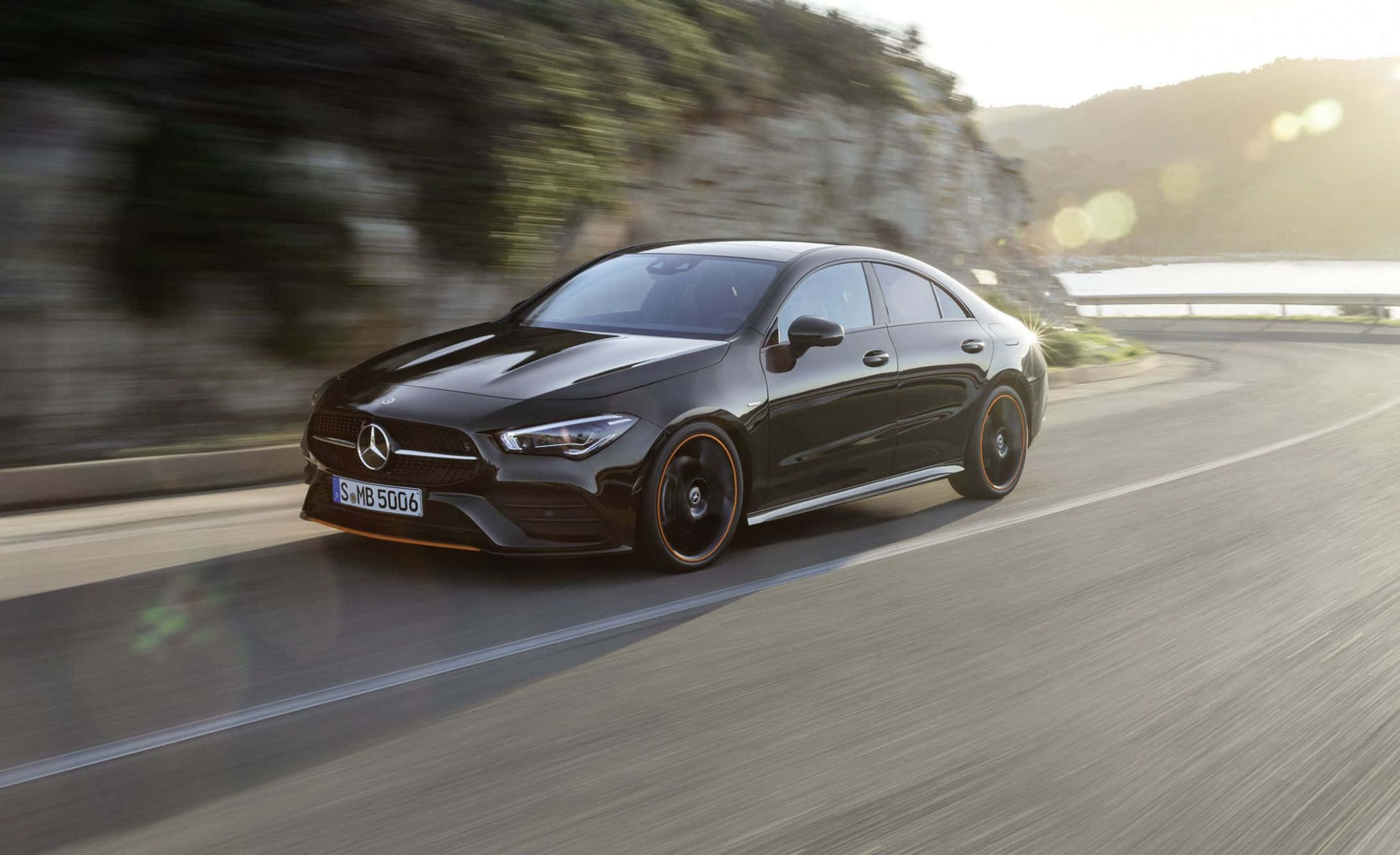 Mercedes Benz Cla-class 桌布 壁紙 — 一架流線型的黑色Mercedes-AMG CLA 35 S E Performance在模糊的綠意和陽光照射下，沿著蜿蜒的海岸道路飛馳。