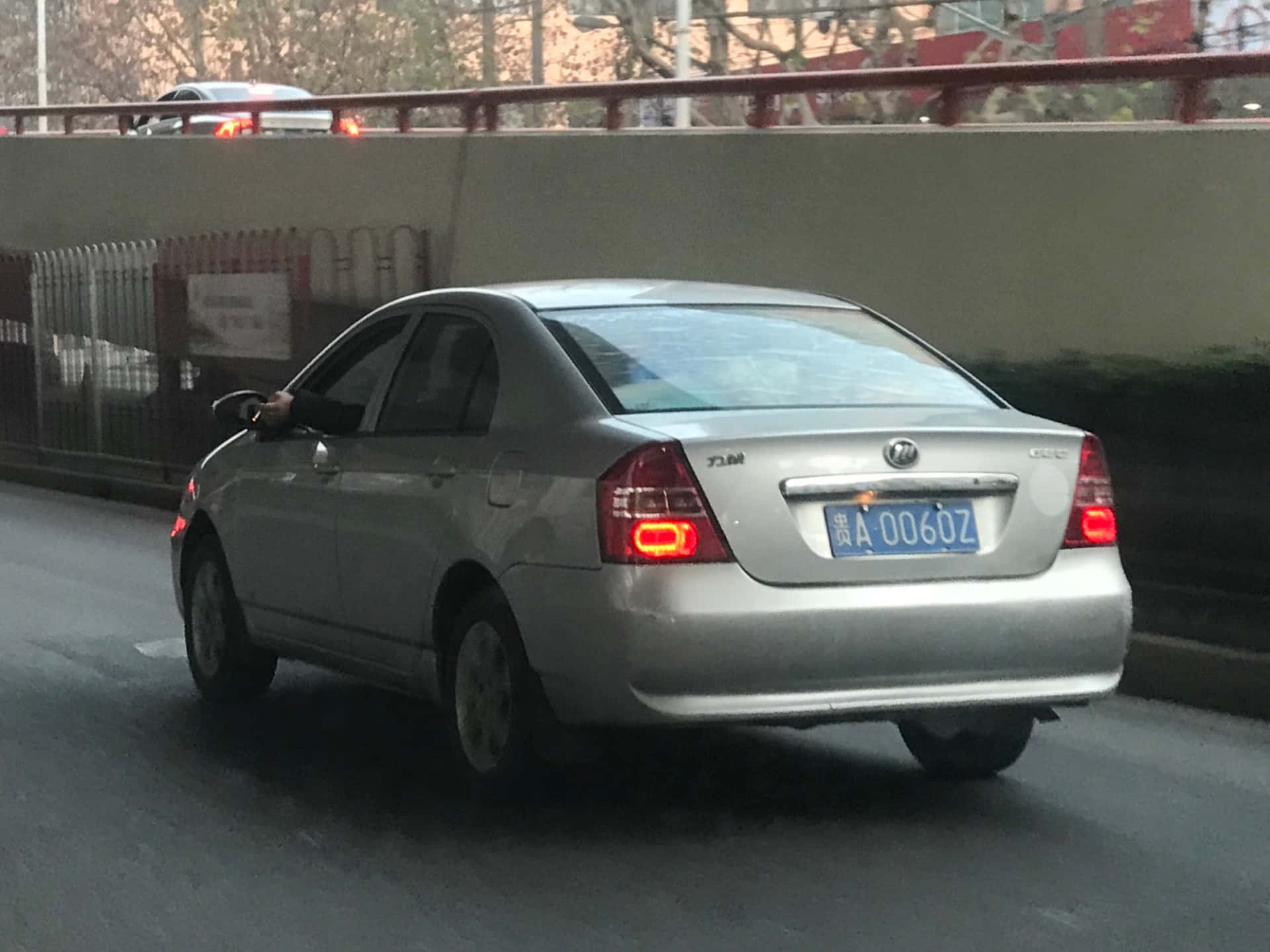  壁紙 — 一輛銀色房車在黃昏時分行駛於城市道路，在天橋下煞車燈亮起。