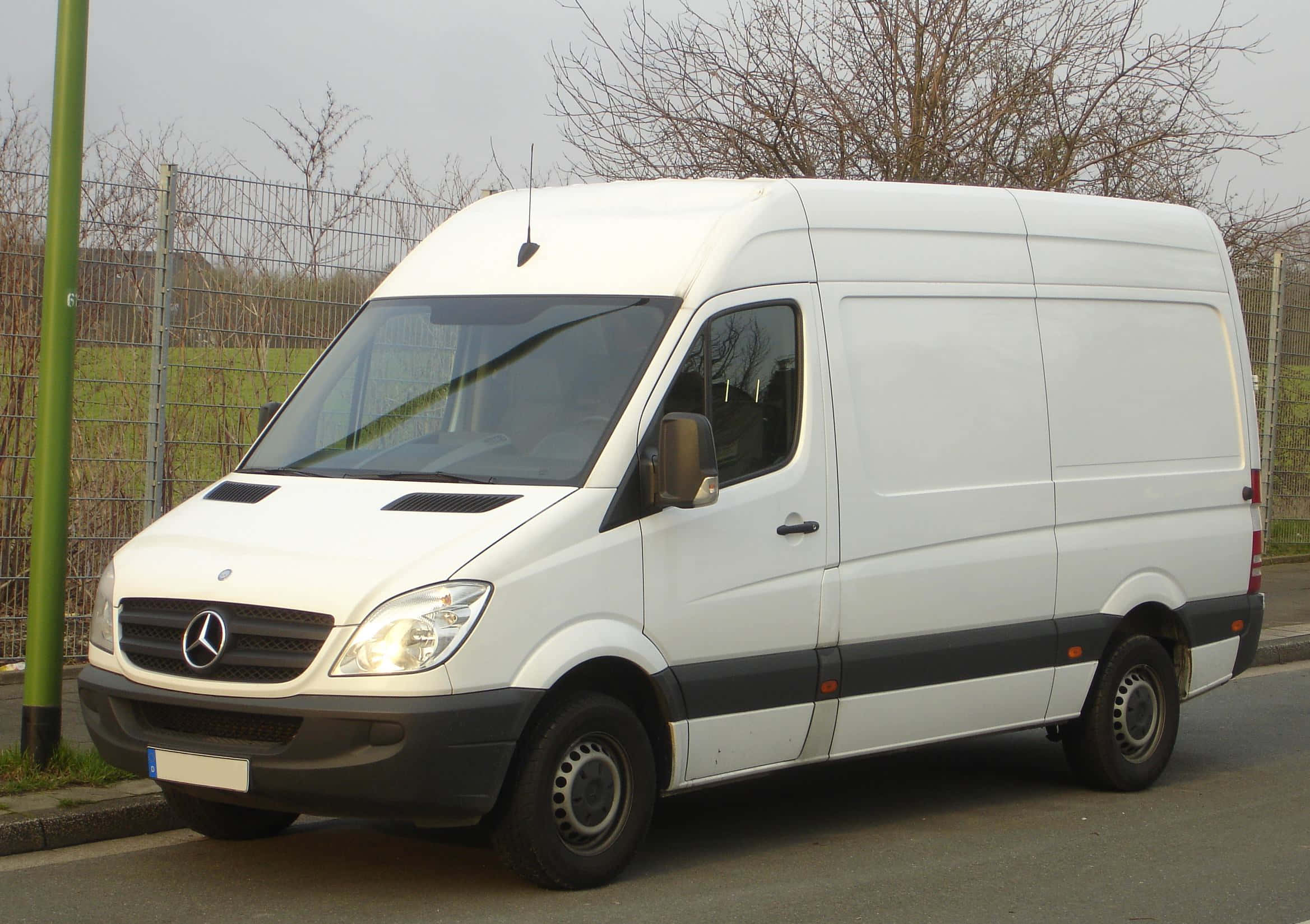 Mercedes Benz Sprinter 桌布 壁紙 — 一輛白色 Mercedes-Benz Sprinter 客貨車停泊在街道上，旁邊有圍欄，背景有光禿禿的樹木。