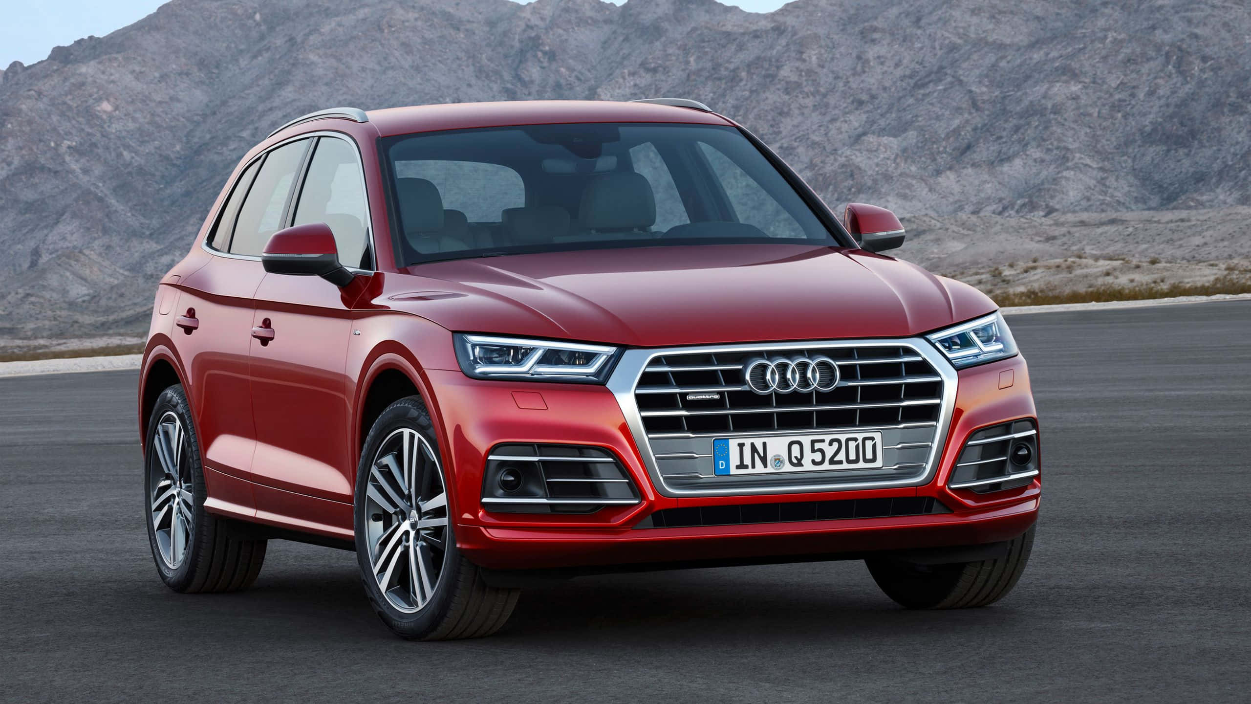 Audi Q5 桌布 壁紙 — 一輛亮紅色的奧迪Q5 SUV停在瀝青路上，背景是岩石山脈，在晴朗的日光下。