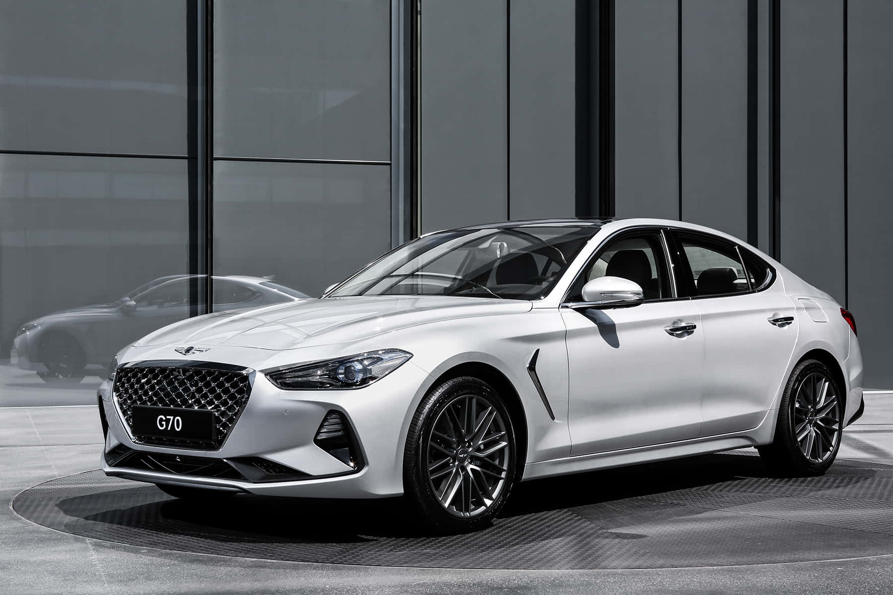 Genesis G70 桌布 壁紙 — 一輛時尚的白色Hyundai G70房車在現代玻璃和鋼鐵背景前，於攝影棚燈光下閃閃發光。
