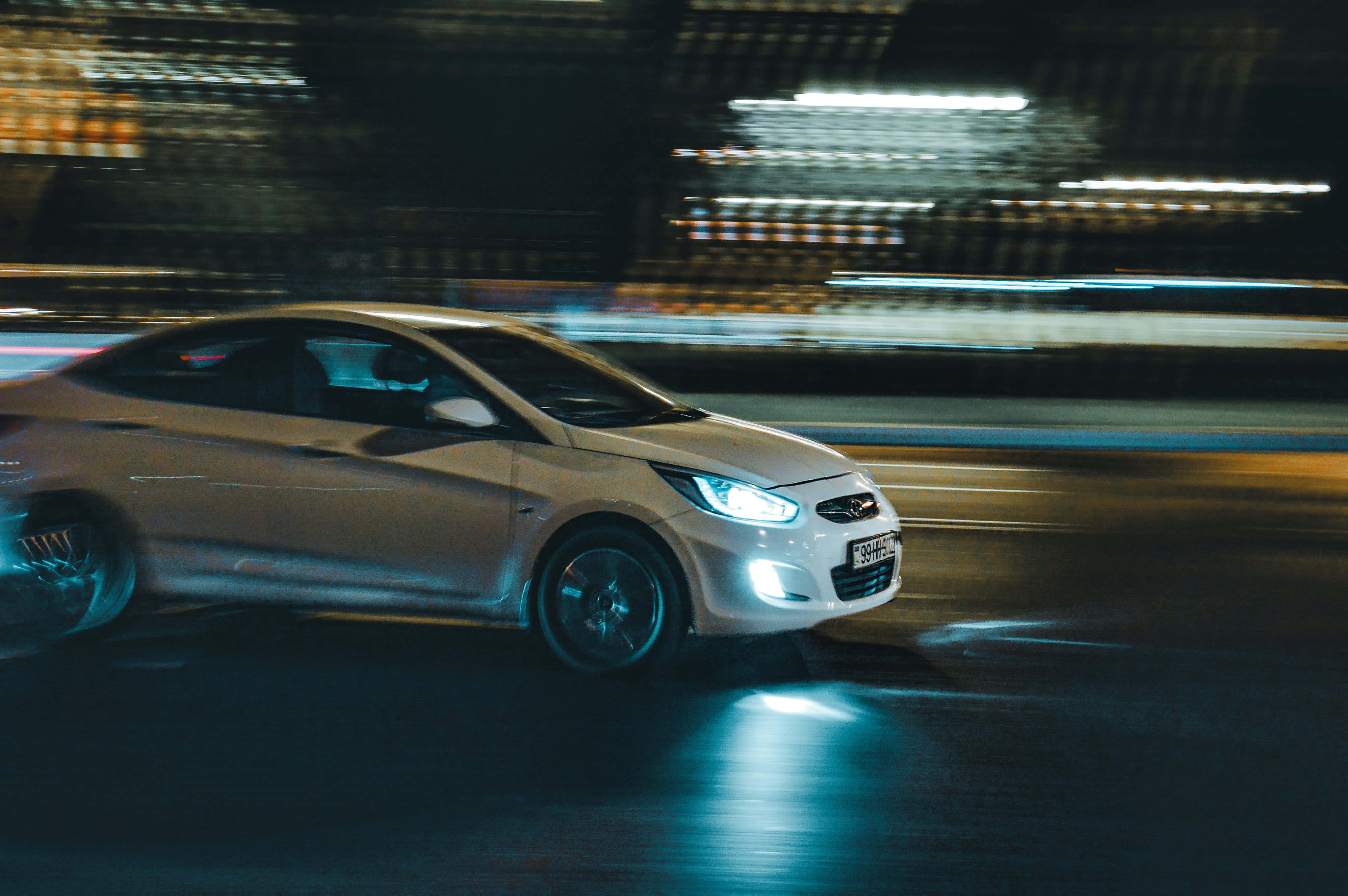 Hyundai Accent 桌布 壁紙 — 一輛銀色轎車在夜晚霓虹燈閃爍的城市中疾馳，光線條紋模糊了都市背景。