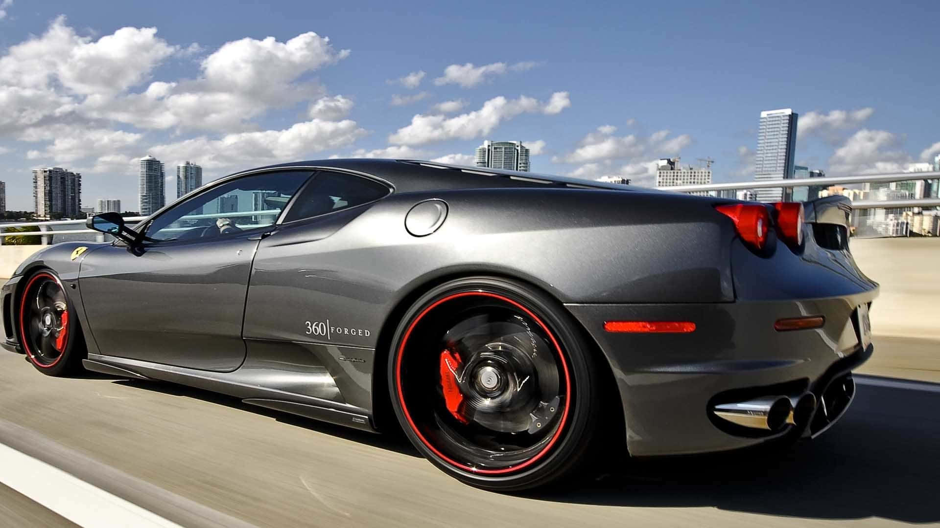 Fantasy Cars 桌布 壁紙 — 一輛流線型啞光灰色法拉利 360 Forged 在晴朗藍天白雲下的城市高速公路上疾馳。