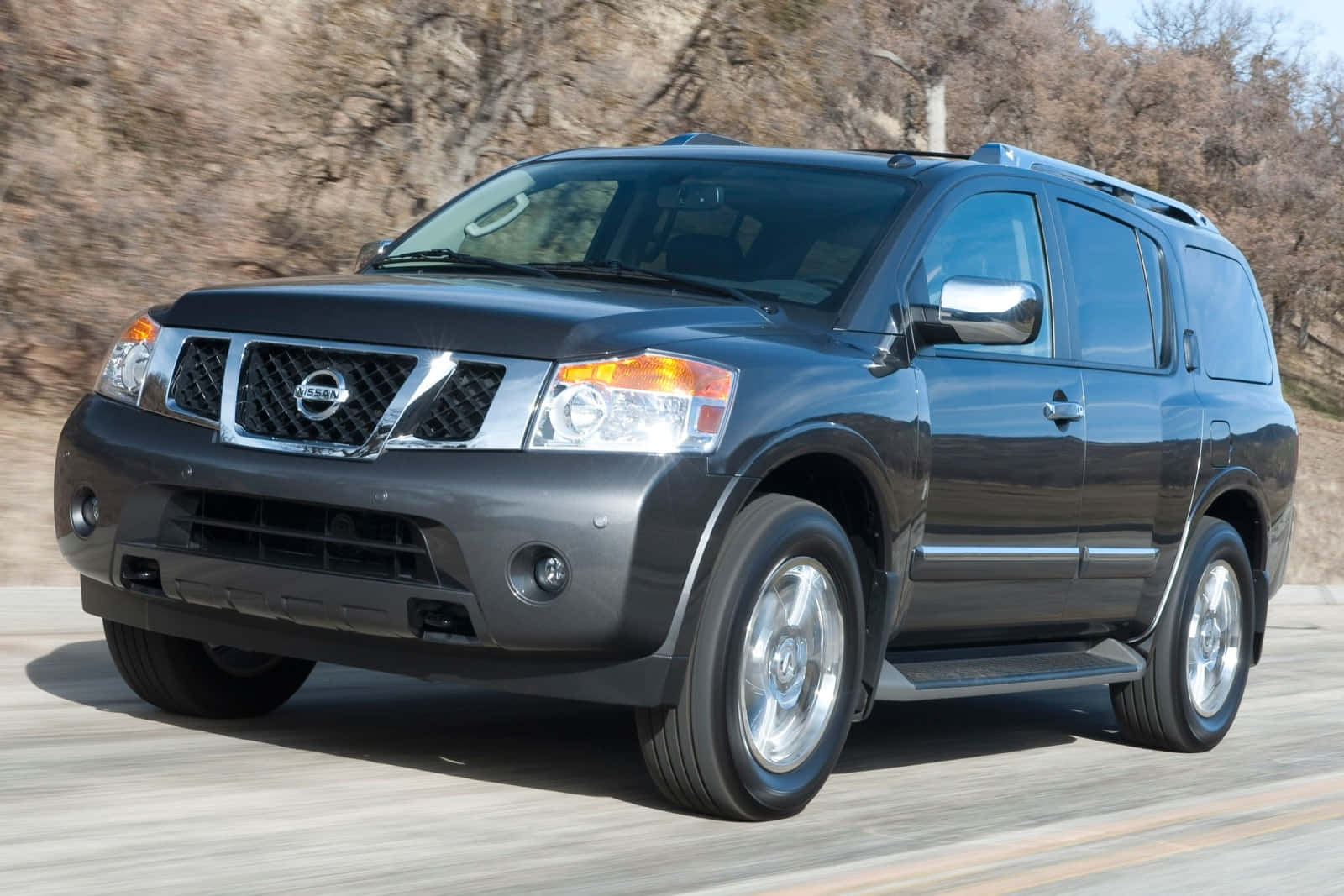 Nissan Armada 桌布 壁紙 — 一輛時尚的深灰色日產SUV在陽光明媚的道路上行駛，背景是模糊的樹木。