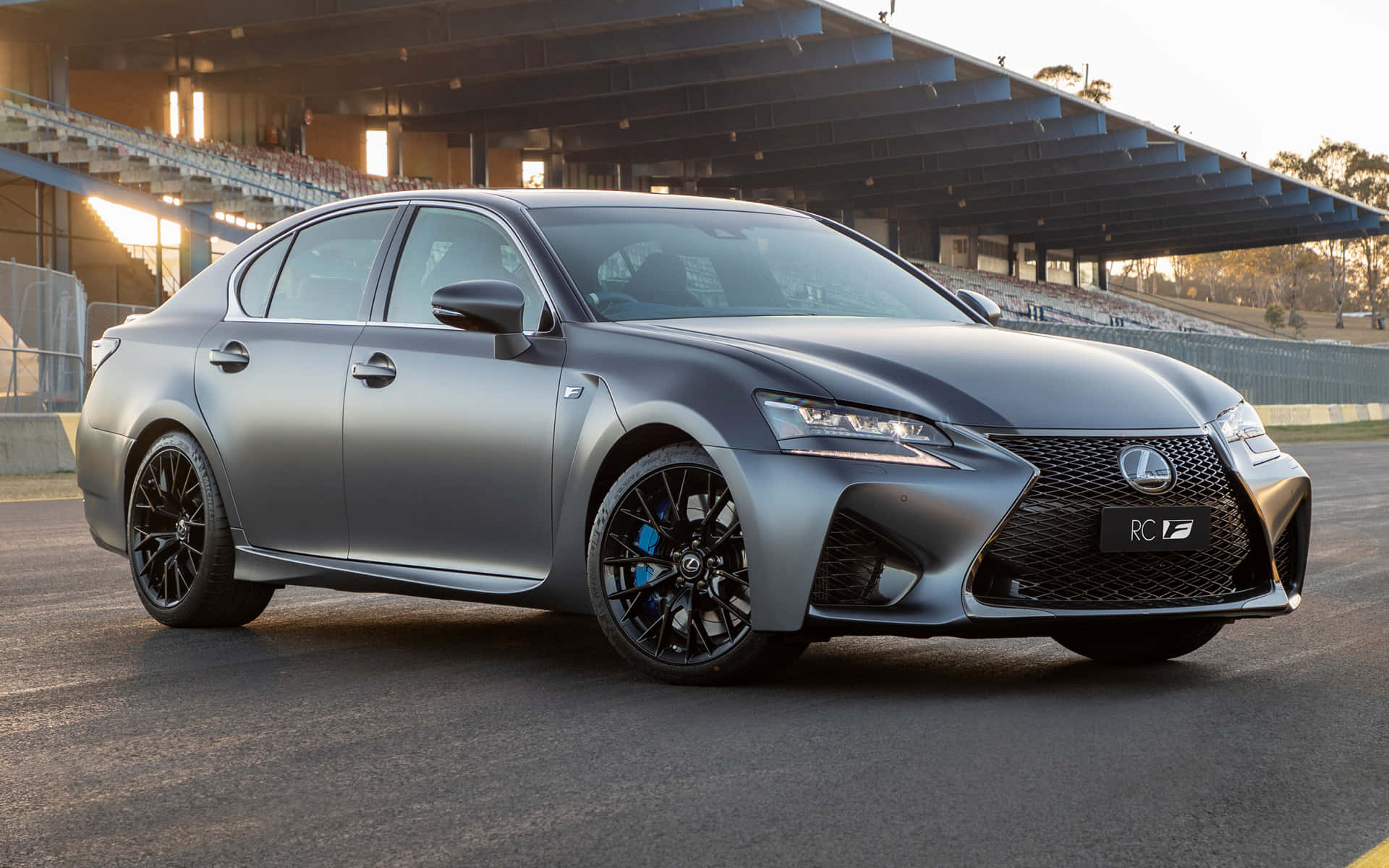 Lexus Gs F 桌布 壁紙 — 一輛時尚的啞光灰色Lexus RC F運動轎車停在賽道上，背景有看台。