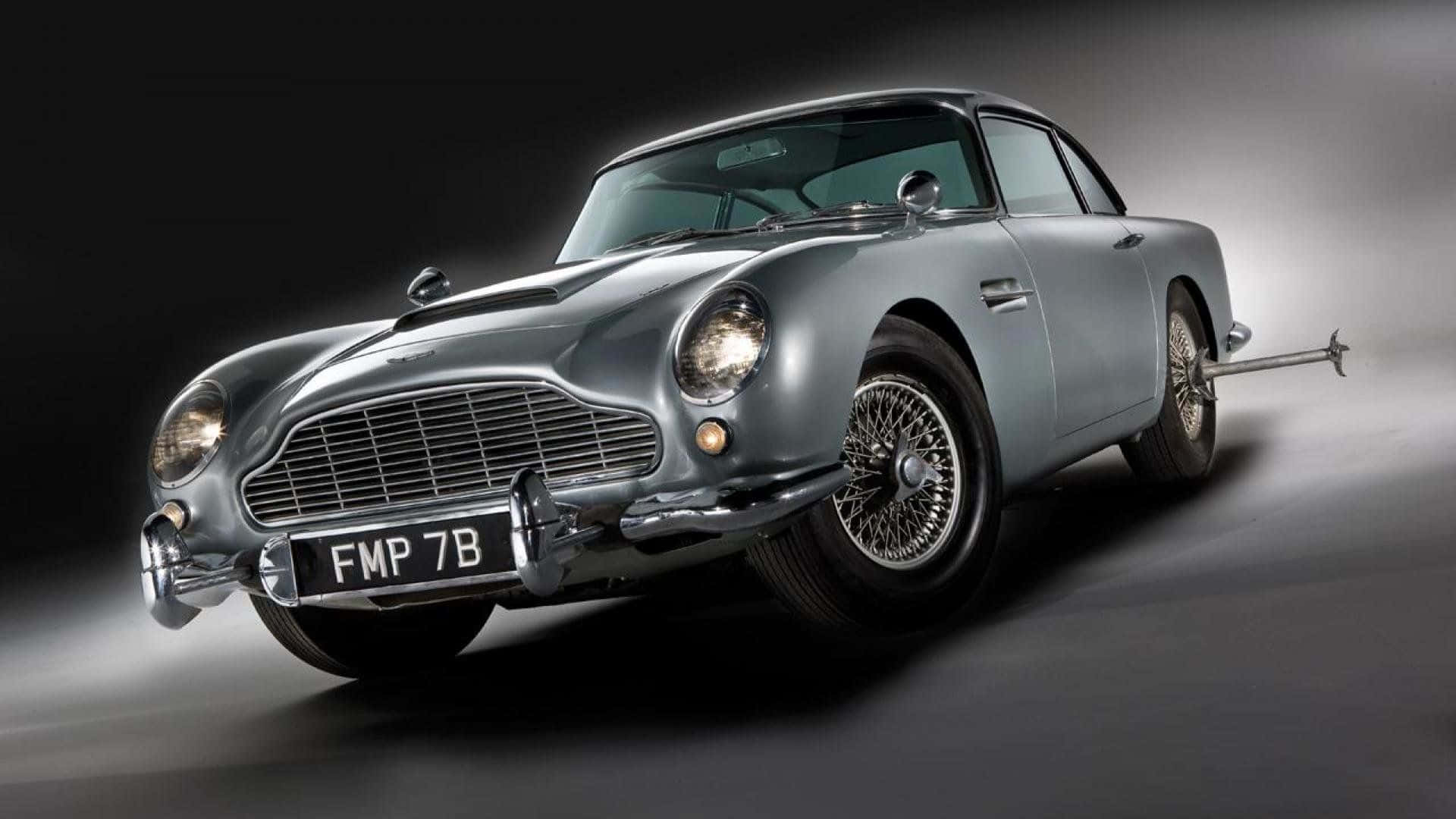 Aston Martin Db5 桌布 壁紙 — 一輛時尚的銀色阿斯頓馬丁DB5在戲劇性的攝影棚燈光下滑行前進，身後留下一道聚光燈軌跡。