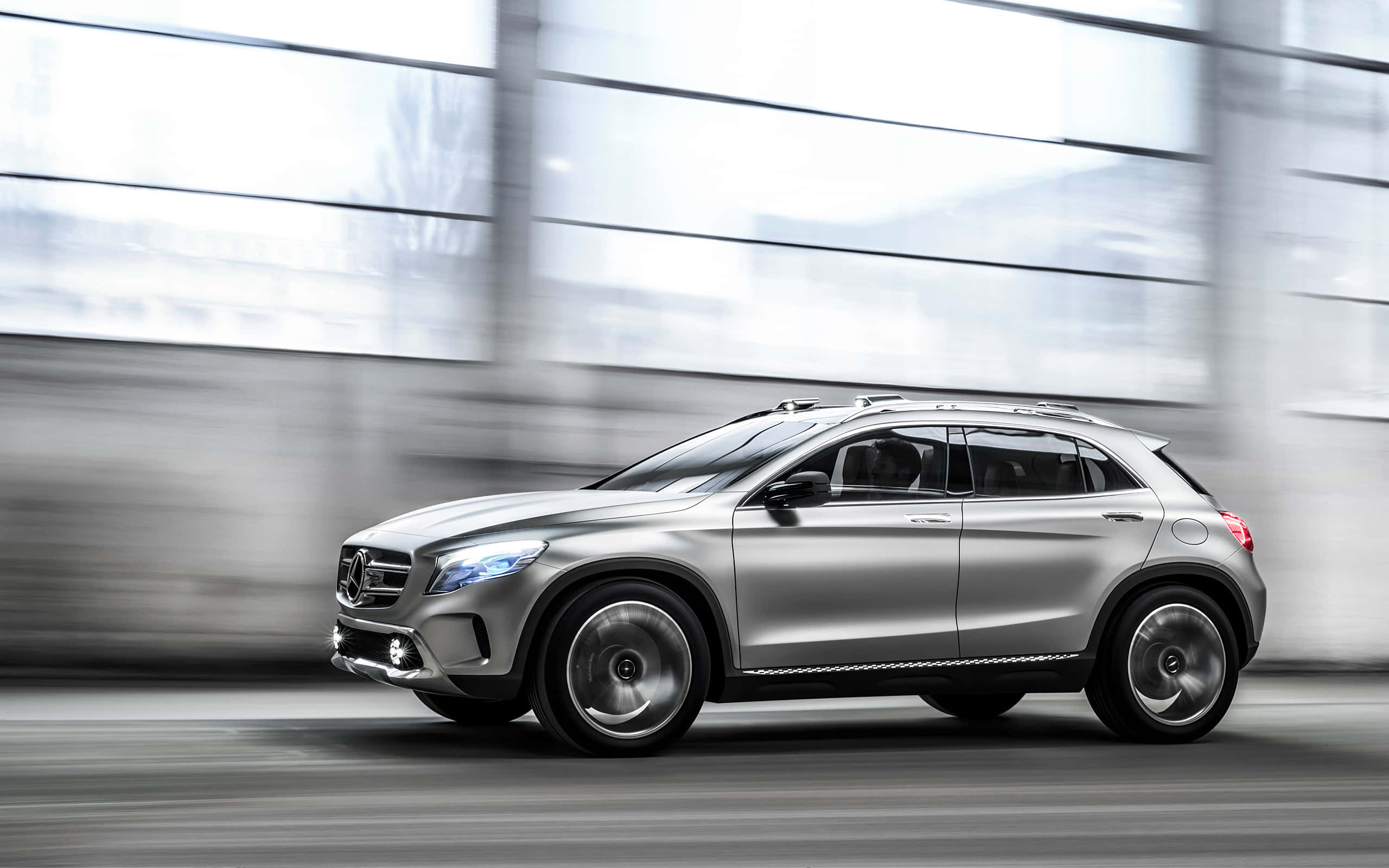 Mercedes Benz Gla-class 桌布 壁紙 — 一輛時尚的銀色SUV高速駛過模糊的現代建築外牆，動態模糊強調了速度。