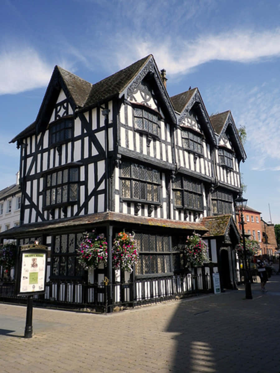 Hereford United Kingdom 桌布 壁紙 — 一座引人注目的黑白木結構建築，帶有華麗的山牆和懸掛的花籃，矗立在明亮的藍天下。