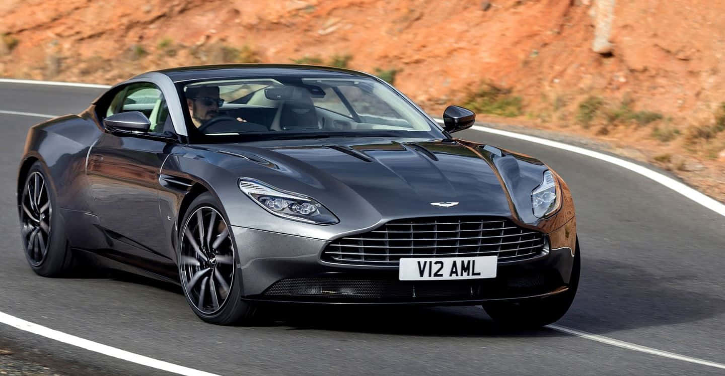 Aston Martin Db11 桌布 壁紙 — 一輛時尚的銀色Aston Martin DB11在蜿蜒的山路上疾馳，背景是紅色岩石峭壁。