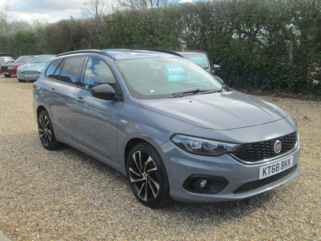 Fiat Tipo 桌布 壁紙 — 一架時尚的銀色Fiat旅行車停泊在碎石上，背景有樹籬，天空多雲。