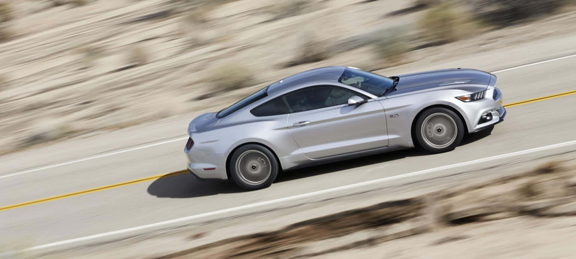 Ford Mustang California Special 桌布 壁紙 — 一輛銀色福特野馬在沙漠公路上疾馳，模糊的環境強調了運動感。