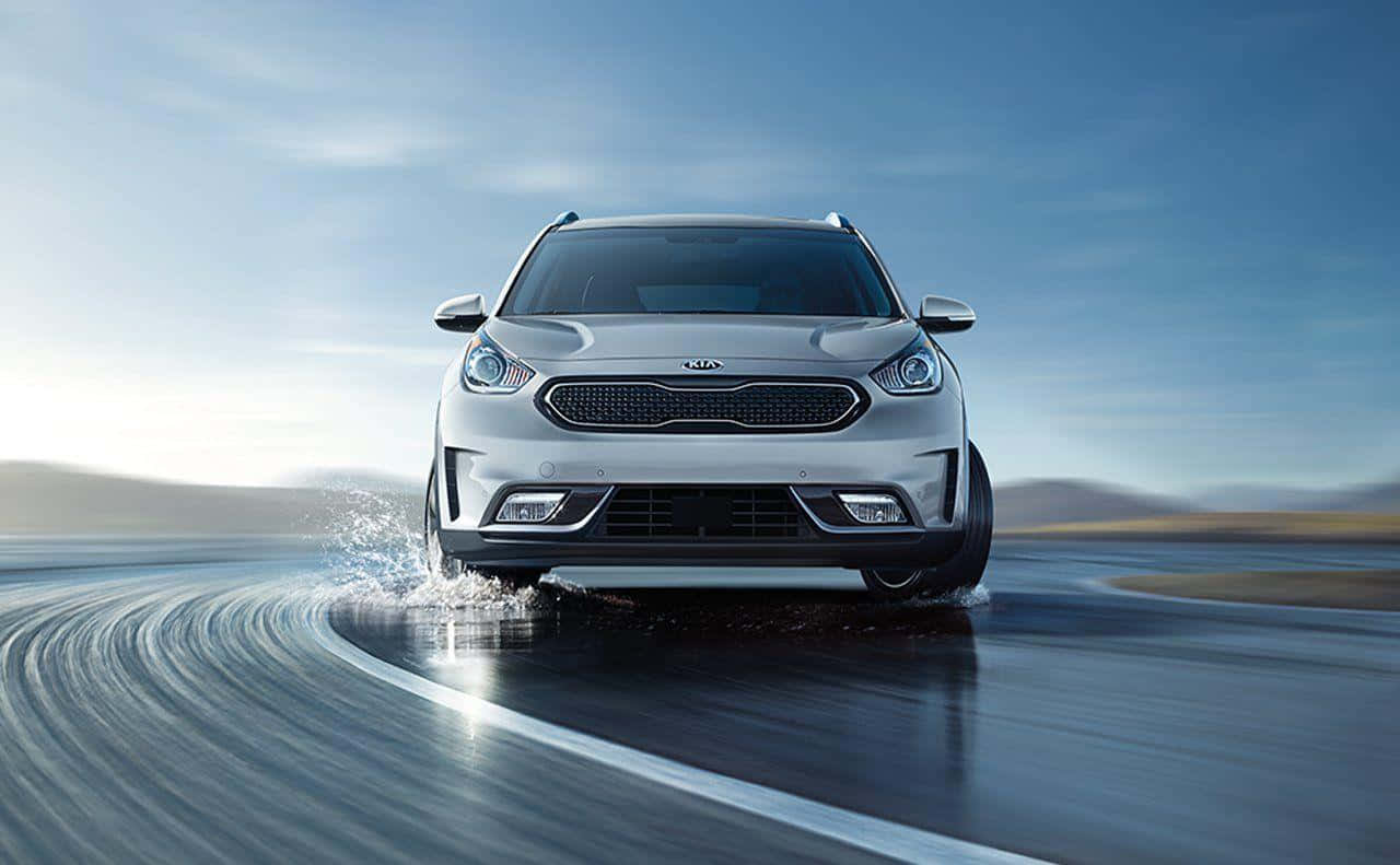 Kia Niro 桌布 壁紙 — 一輛銀色Kia SUV在晴朗藍天下，飛馳在濕滑的沙漠公路上，濺起水花。