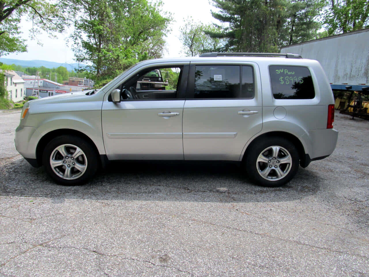 Honda Pilot 桌布 壁紙 — 銀色SUV停泊在裂開的瀝青路上，背景有樹木和遠山，在明亮日光下。