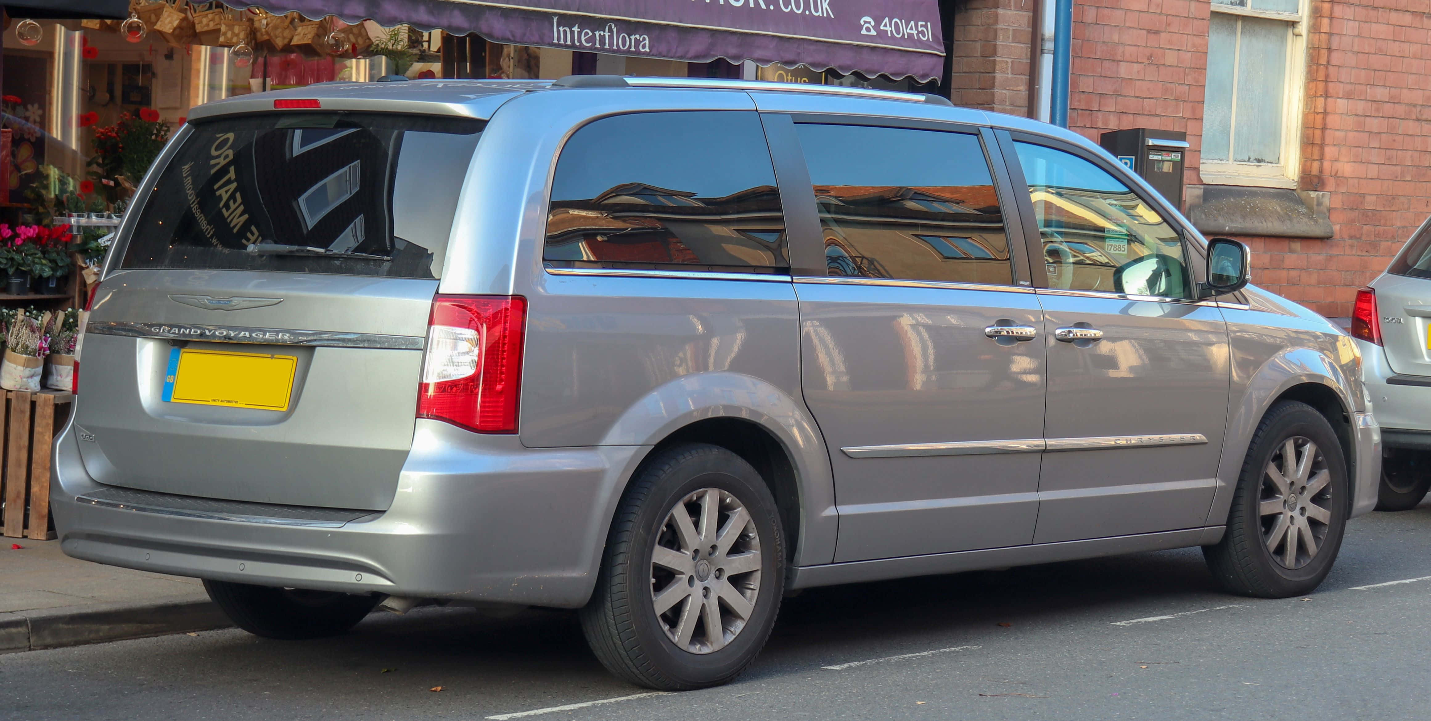 Chrysler Voyager 桌布 壁紙 — 銀色小型貨車停泊在城市街道上，旁邊是磚砌建築物，帶有花店簷篷。