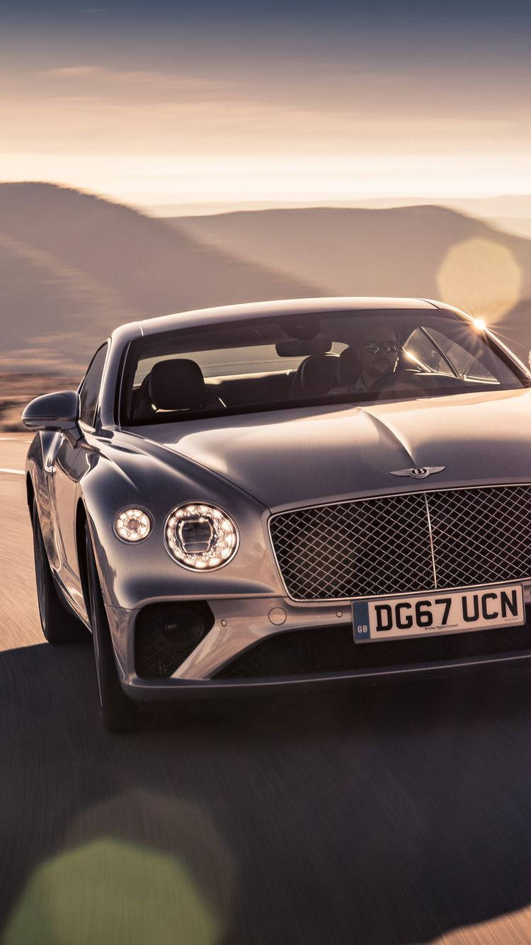 銀色賓利 Continental GT 在金色日落下的沙漠公路上疾馳。