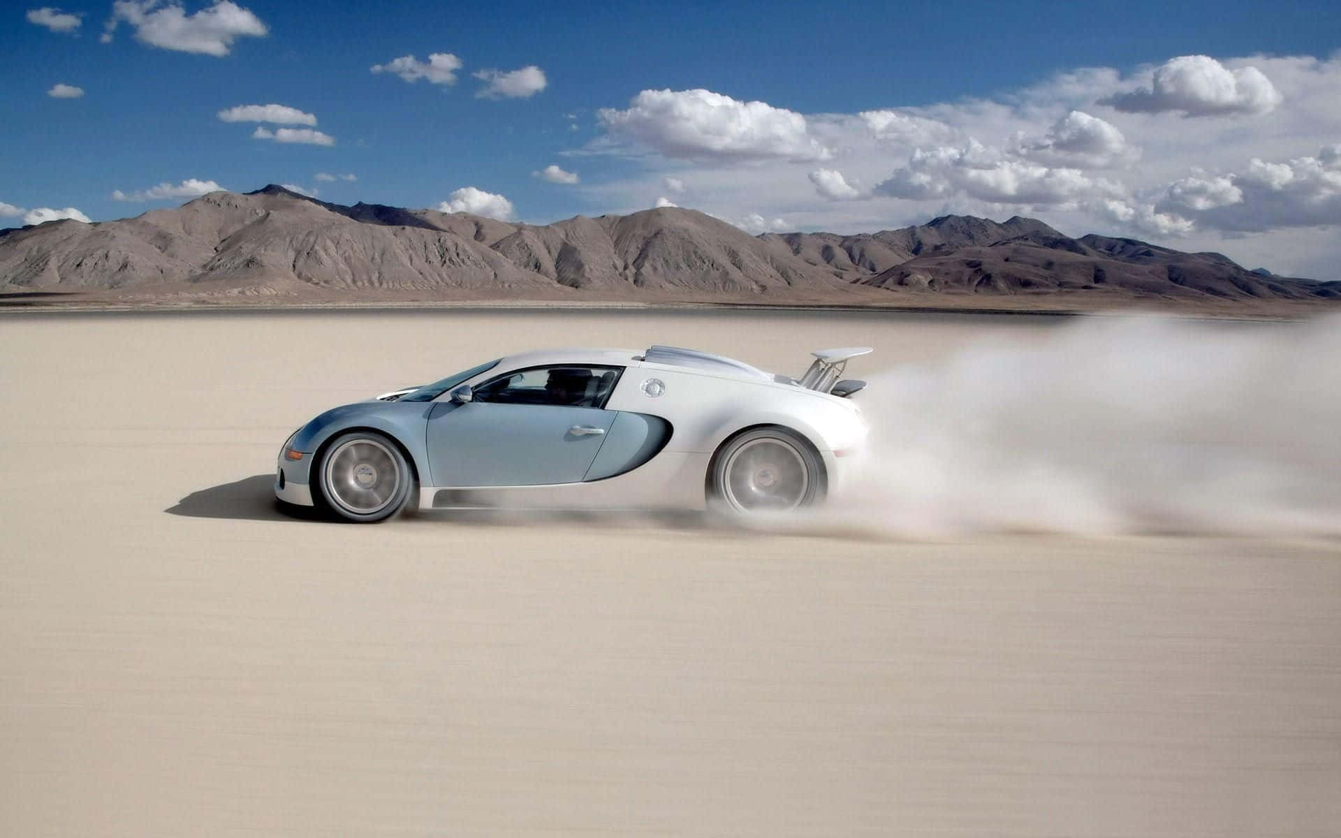 Bugatti Veyron 桌布 壁紙 — 一輛銀色Bugatti超級跑車在廣闊的沙漠乾涸湖床上飄移，揚起灰塵，天空湛藍，白雲點綴。