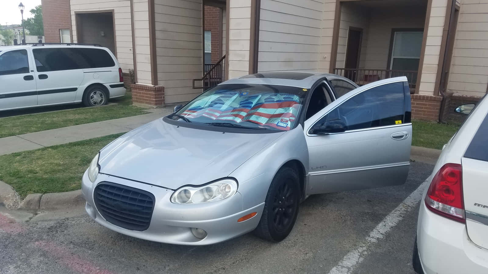Chrysler Lhs 桌布 壁紙 — 一架銀色克萊斯勒Sebring，司機門打開，美國國旗披在擋風玻璃上，停在住宅區。