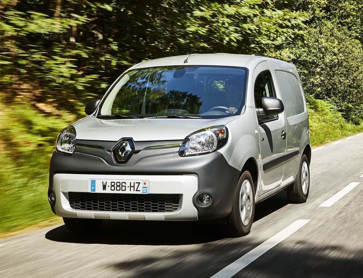Renault Kangoo 桌布 壁紙 — 一輛銀色雷諾Kangoo客貨車在陽光明媚的林間道路上疾馳，綠色樹葉呈現動態模糊效果。