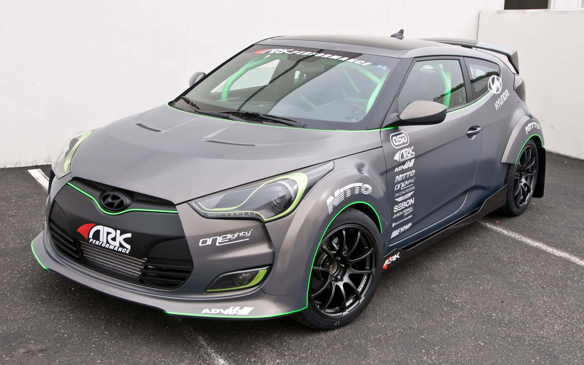 Hyundai Veloster 桌布 壁紙 — 一架啞光灰色現代Veloster賽車，帶有螢光綠色點綴和贊助商貼紙，停泊在停車場。