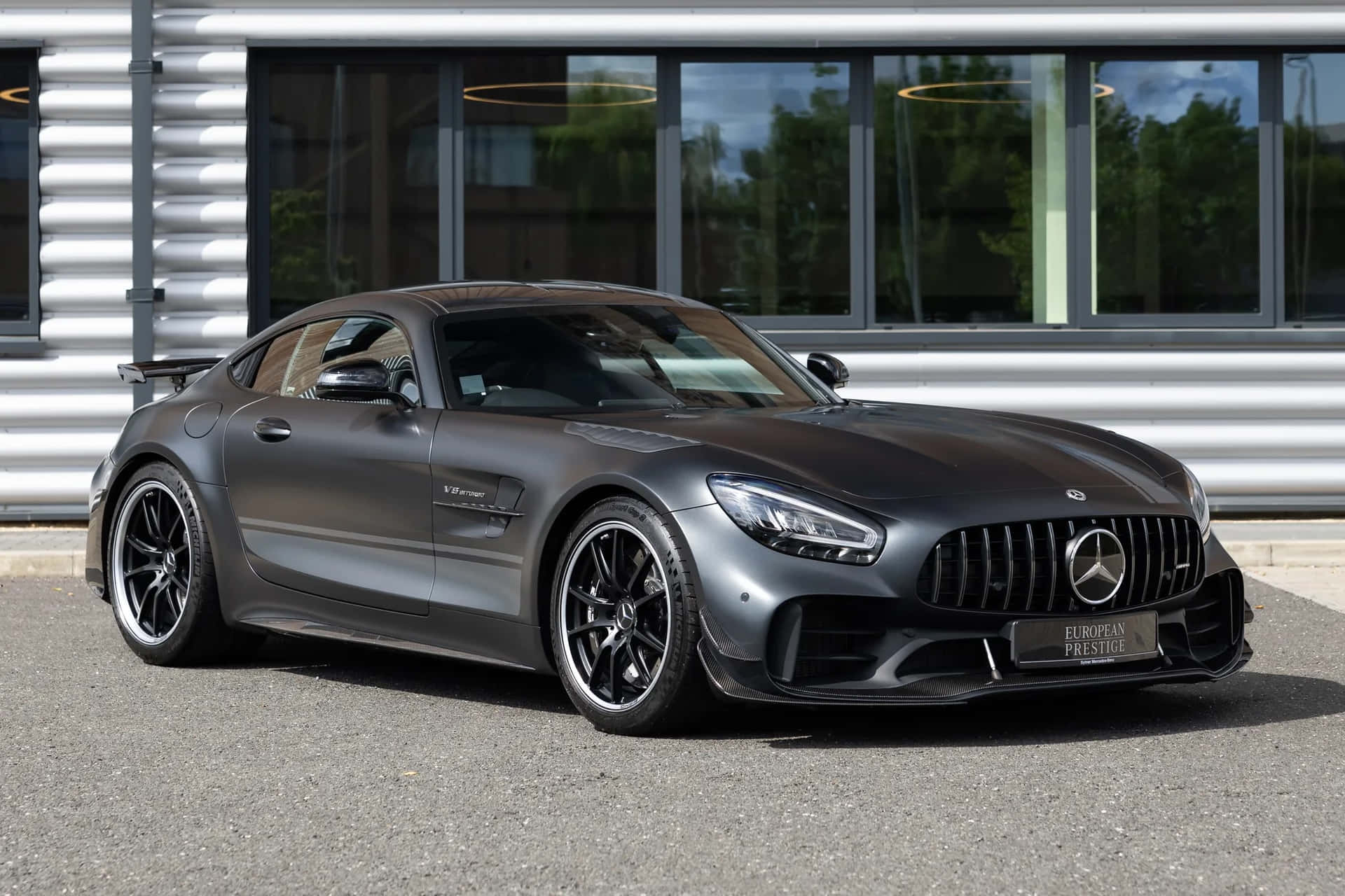  壁紙 — 一架時尚的啞光灰色 Mercedes-AMG GT R 跑車停泊在現代建築前，建築物有大窗戶。