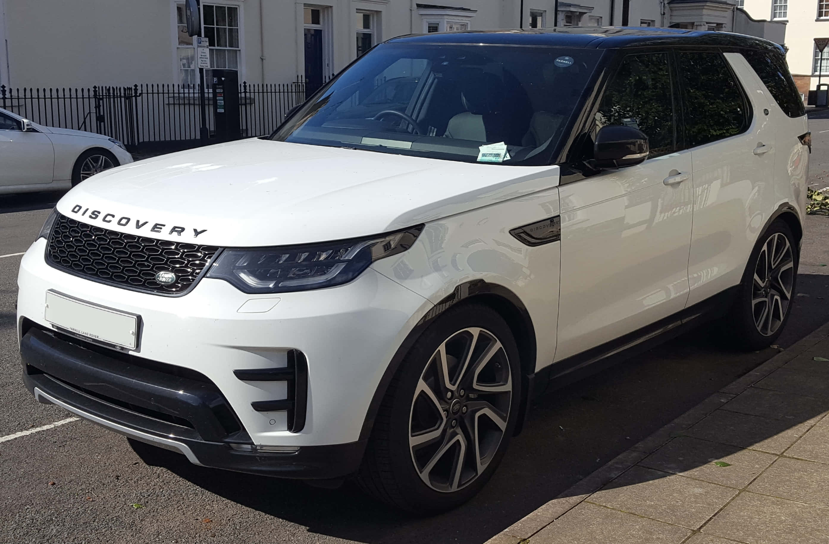 Land Rover Discovery 桌布 壁紙 — 一輛純白色的 Land Rover Discovery SUV 停泊在陽光明媚的城市街道上，背景是經典建築。
