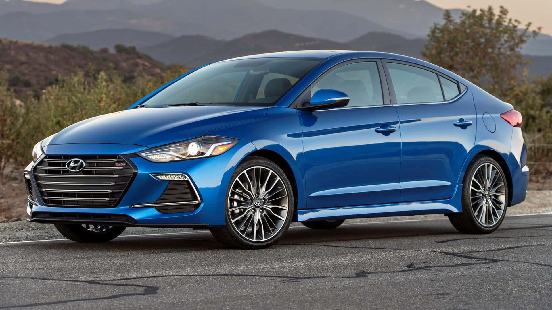 Hyundai Elantra 桌布 壁紙 — 一輛充滿活力的藍色現代伊蘭特轎車在沙漠公路上，在金色時光的光線下閃閃發光，遠處有山脈。