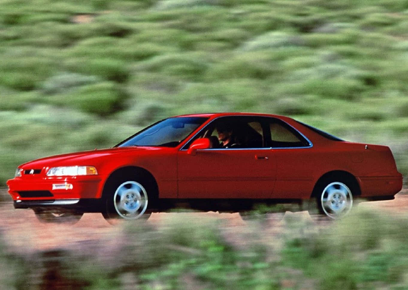 Acura Legend 桌布 壁紙 — 一輛充滿活力的紅色運動型轎跑車在泥濘道路上疾馳，模糊的綠色樹葉從旁掠過。