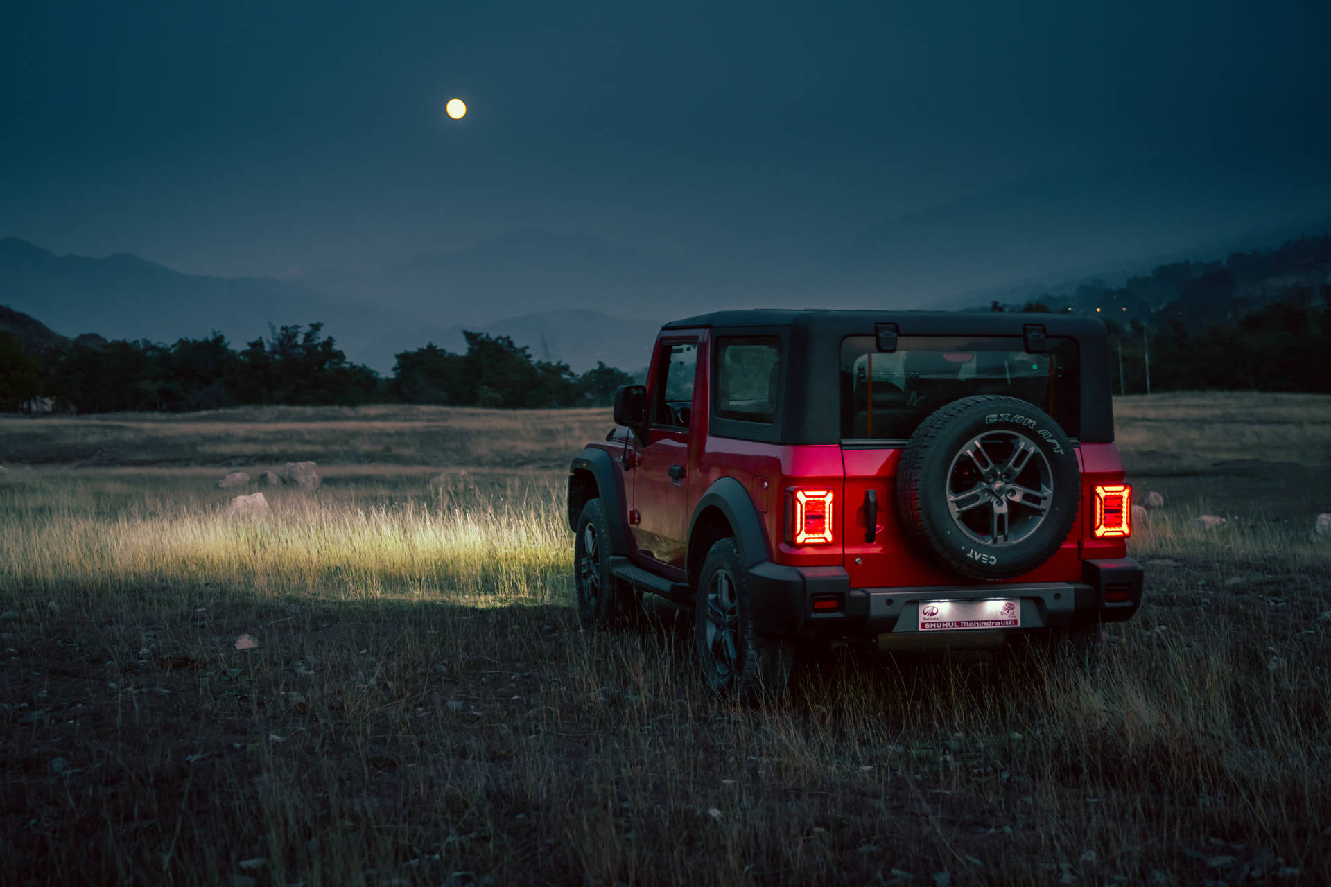 紅色Jeep Wrangler在黃昏滿月下停泊在田野中。