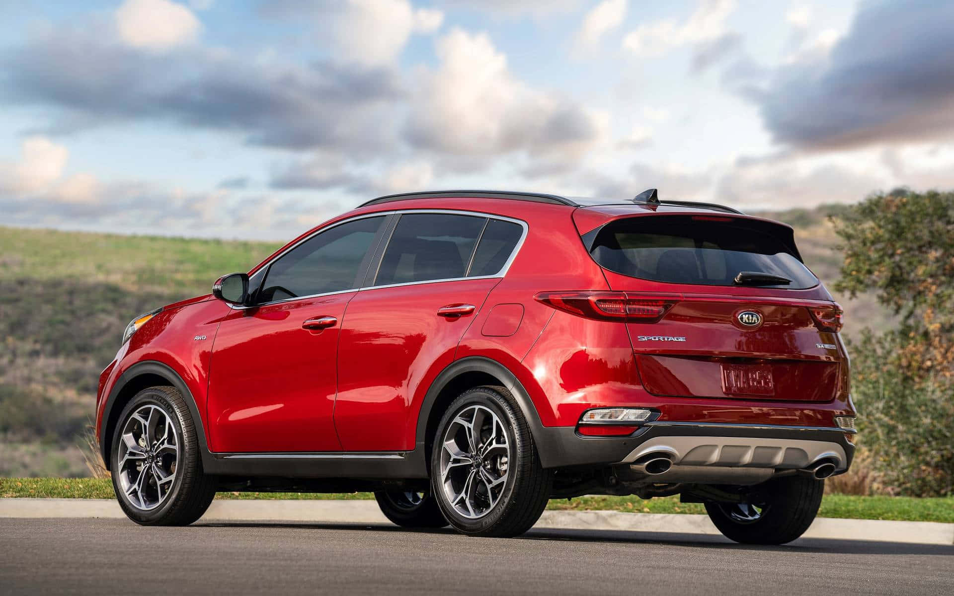 Kia Sportage 桌布 壁紙 — 一輛亮紅色Kia Sportage SUV停泊在路邊，背景是起伏的丘陵和多雲的天空。