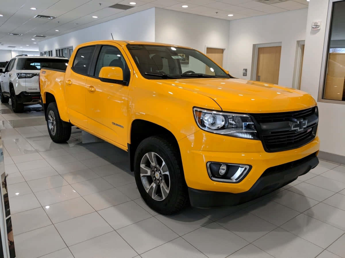 Gmc Canyon 桌布 壁紙 — 一輛亮黃色的雪佛蘭 Colorado 皮卡車在展廳燈光下，在拋光瓷磚地板上閃閃發光。