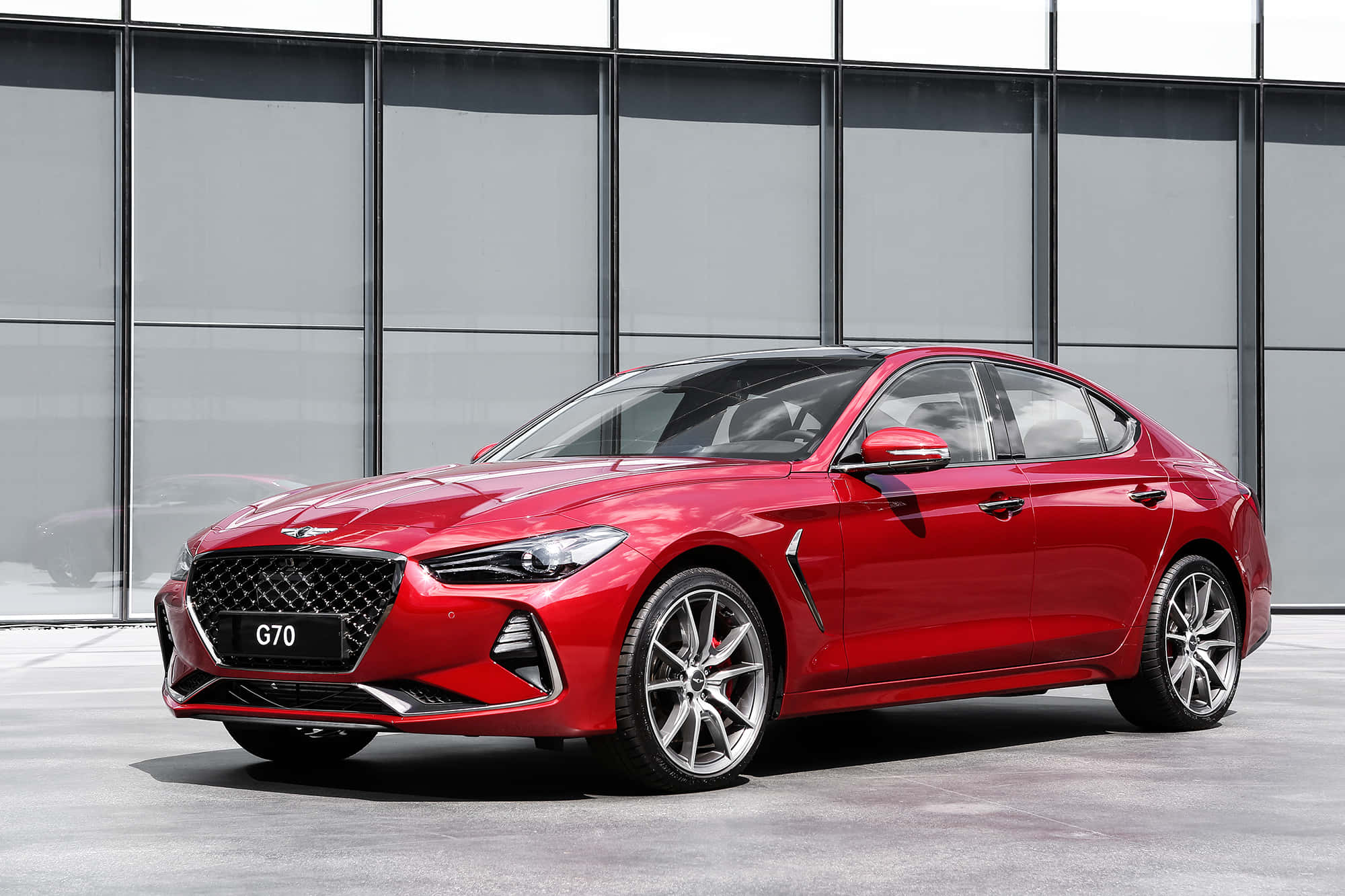 Genesis G70 桌布 壁紙 — 一輛亮紅色的現代 G70 房車停在現代玻璃建築前，在明亮的日光下。