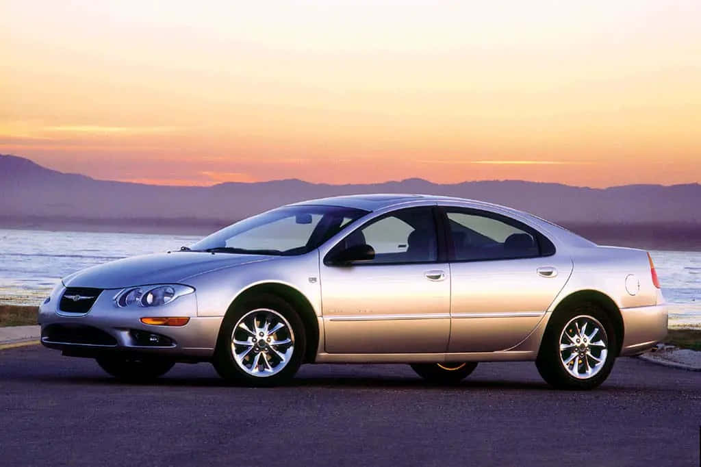 Chrysler Lhs 桌布 壁紙 — 一輛銀色房車在日落時停泊在行人路上，背景有山和水。