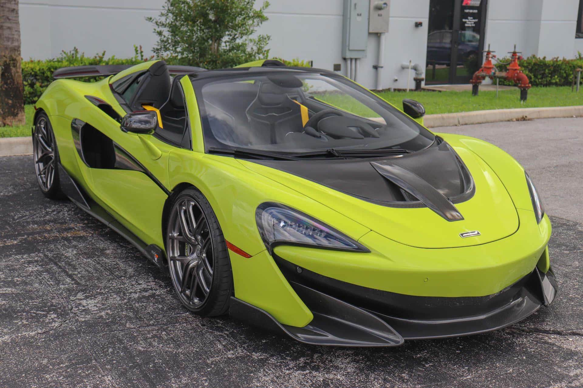 Mclaren 600lt Spider 桌布 壁紙 — 一輛充滿活力的青檸綠色McLaren跑車，帶有黑色飾邊，停泊在建築物和綠化附近的瀝青路面上。