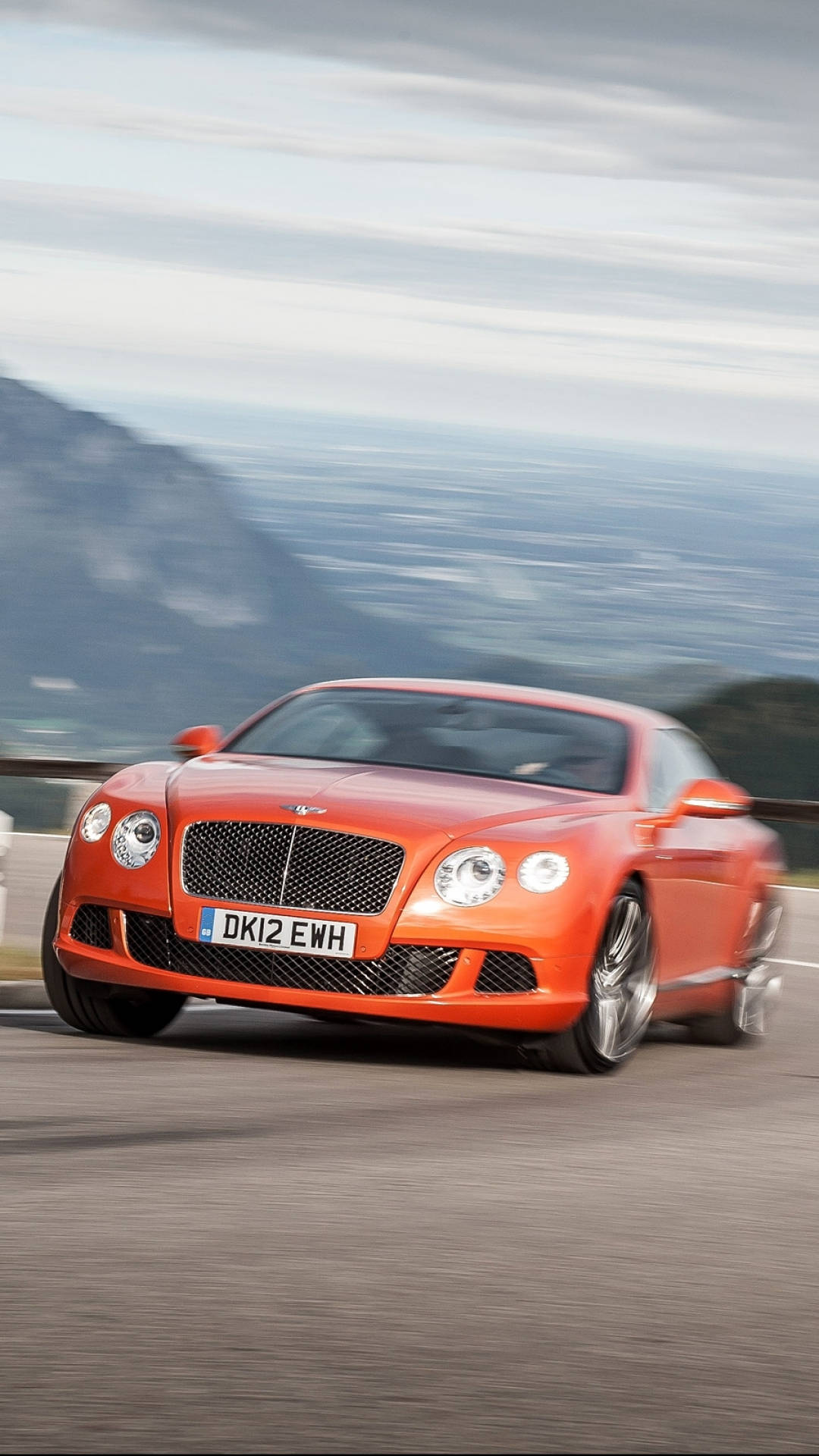 橙色 Bentley 跑車在模糊背景下的山路上疾馳。